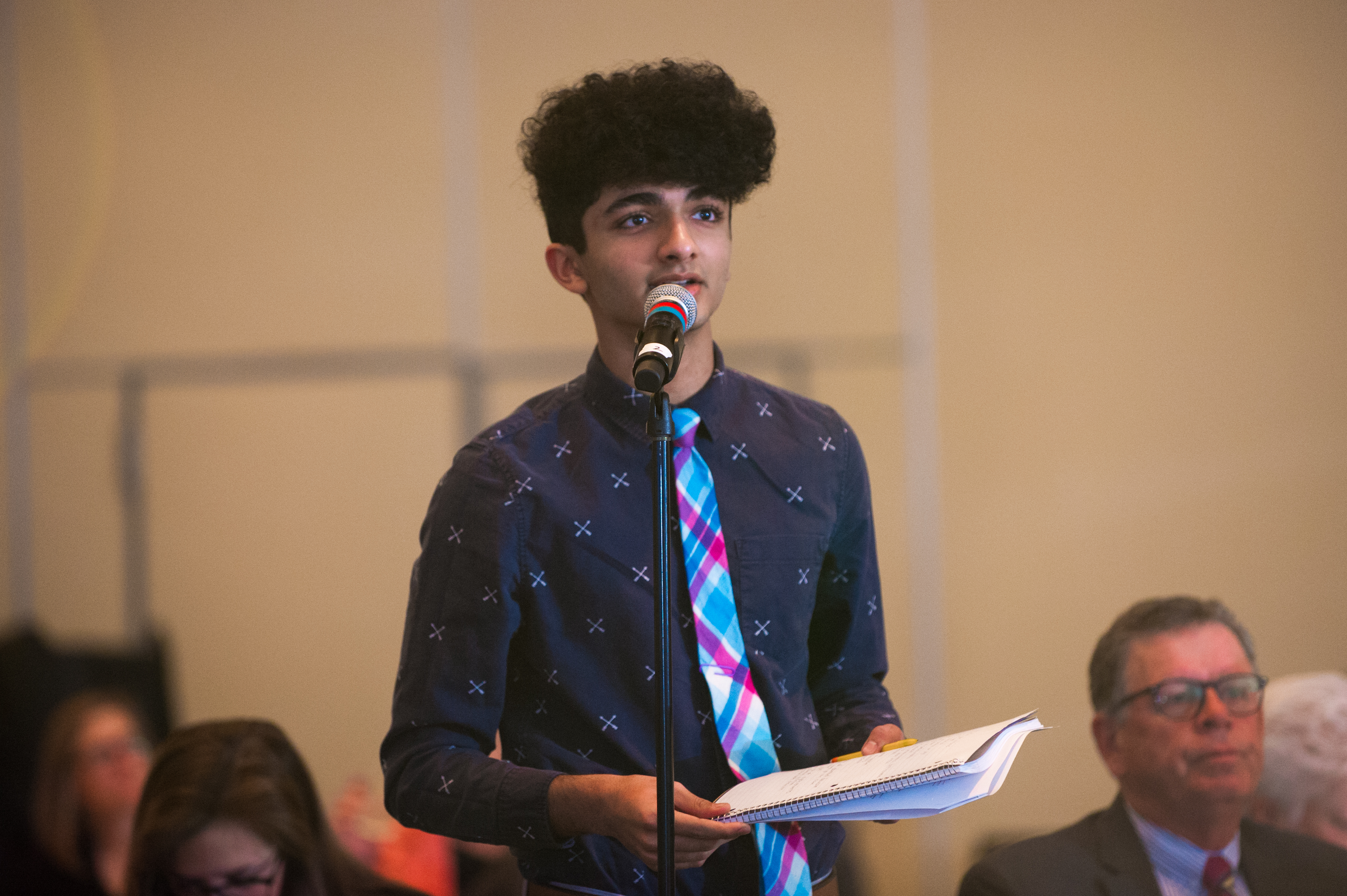 Teen speaking at a microphone with papers in hand