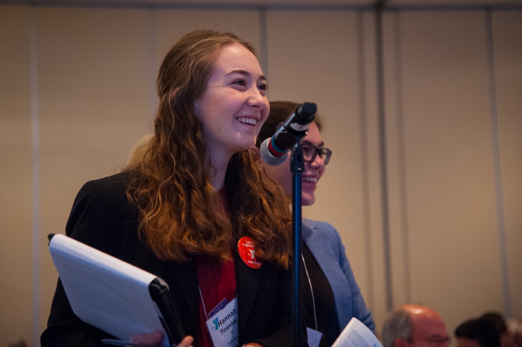 Teenage stands at a microphone holding a clipboard
