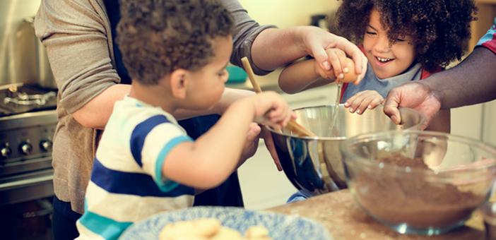 Parents helping children crack eggs into a bowl while baking