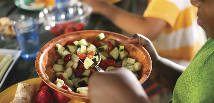 Person scooping tomato cucumber salad out of a wooden bowl