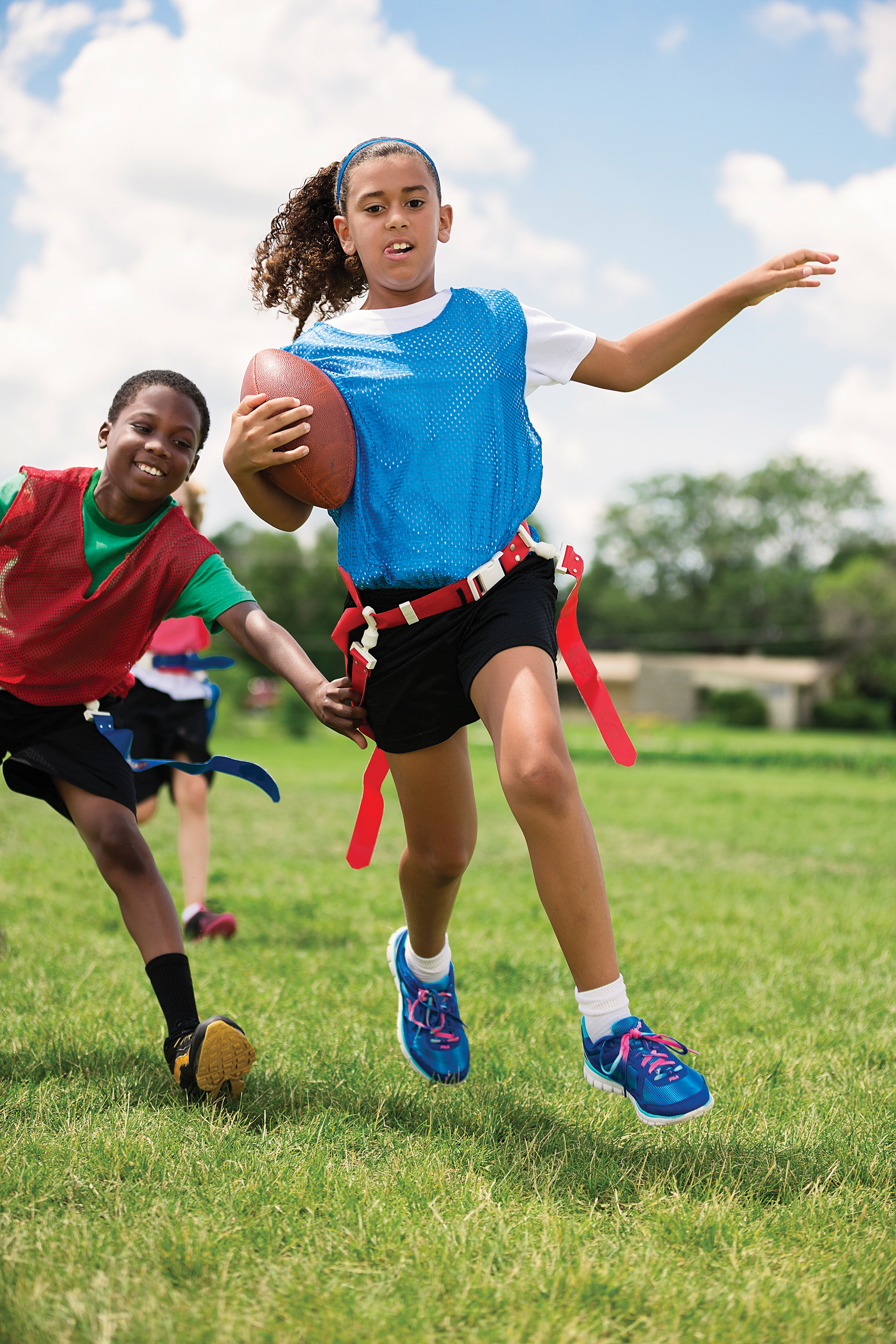 Girl running with football while boy chases during a game of flag football - YMCA