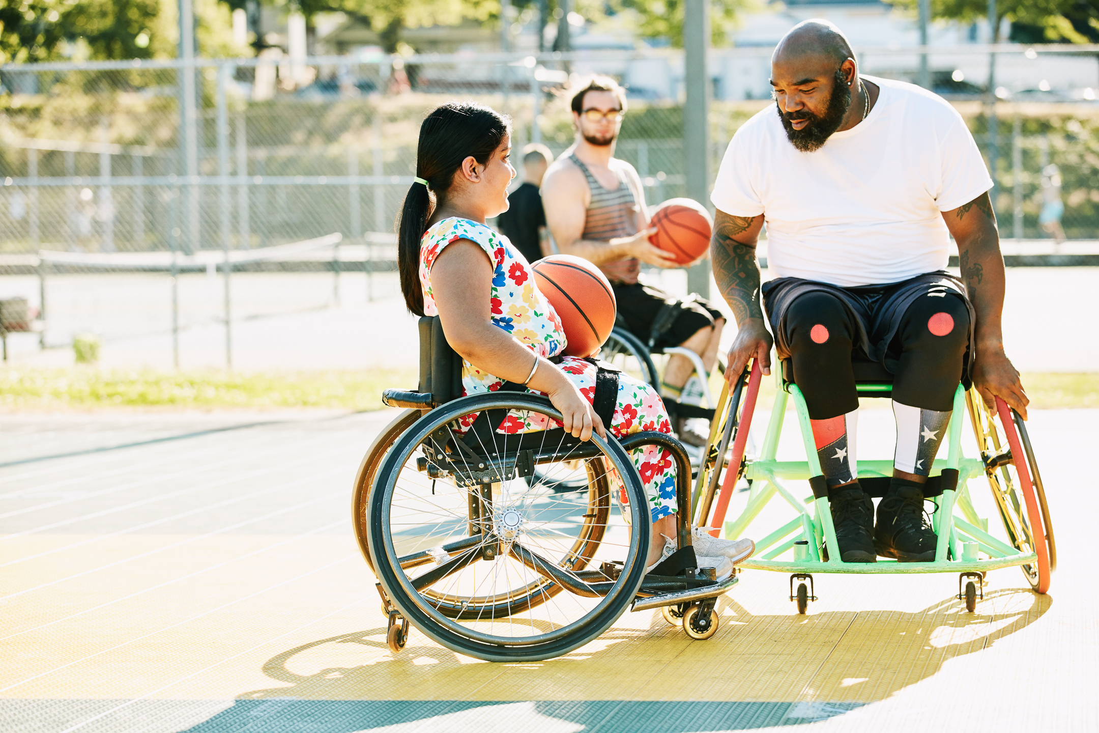  Smiling young female adaptive athlete getting advice from adaptive basketball coach during practice on summer evening 