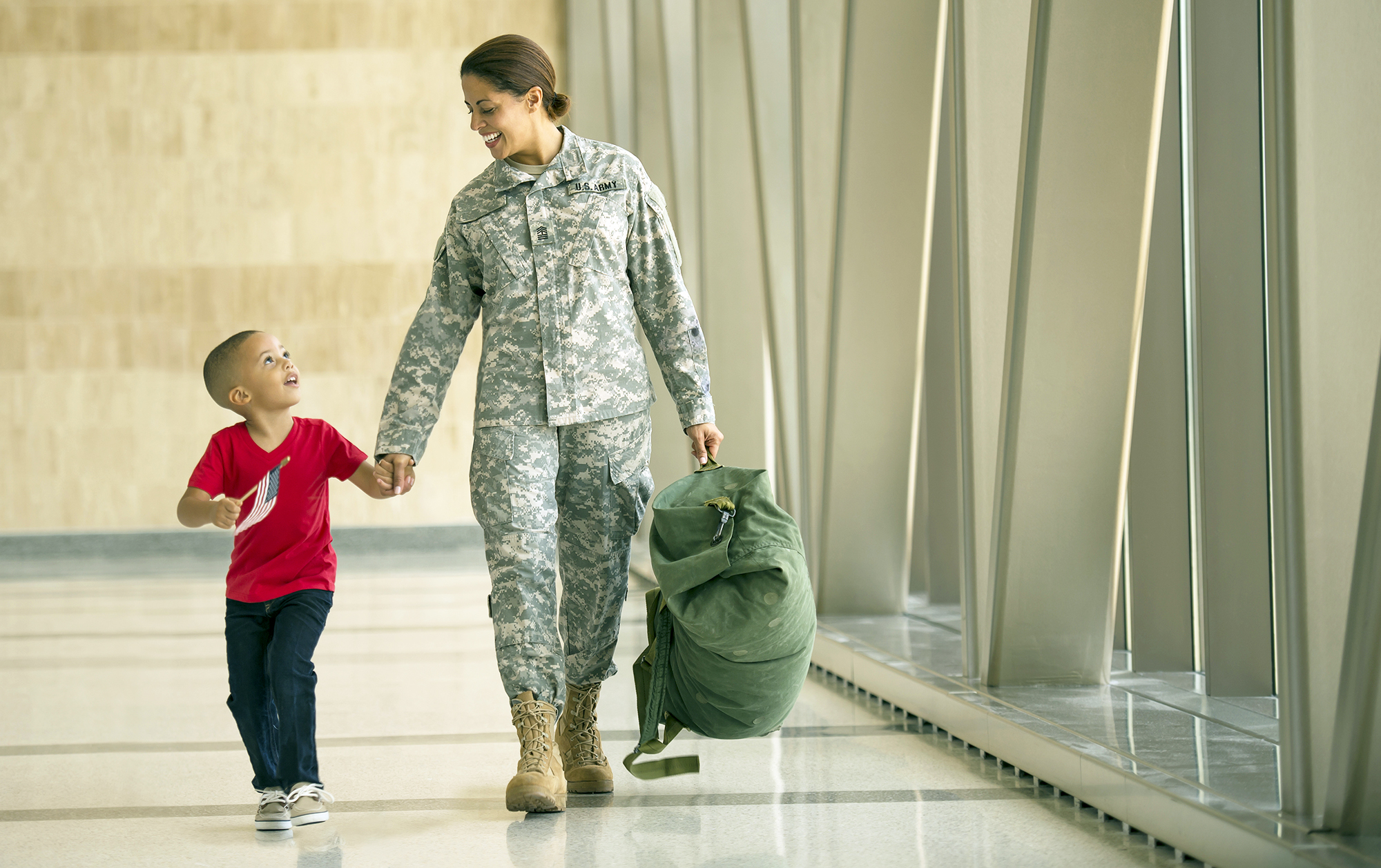 Woman in army fatigues walking through a hallway holding the hand of a young boy