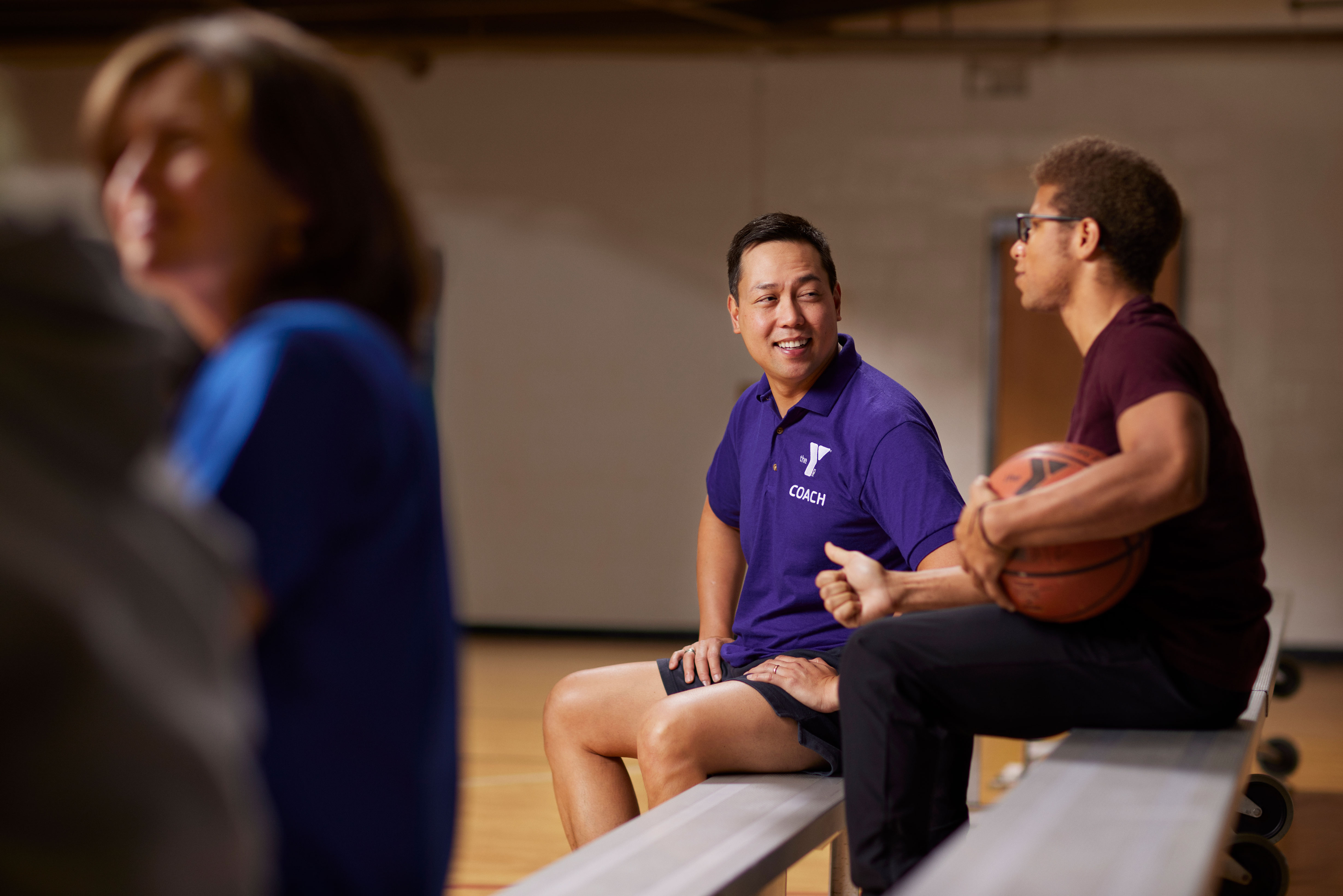 Y coach chatting with male teen on bleachers in gym