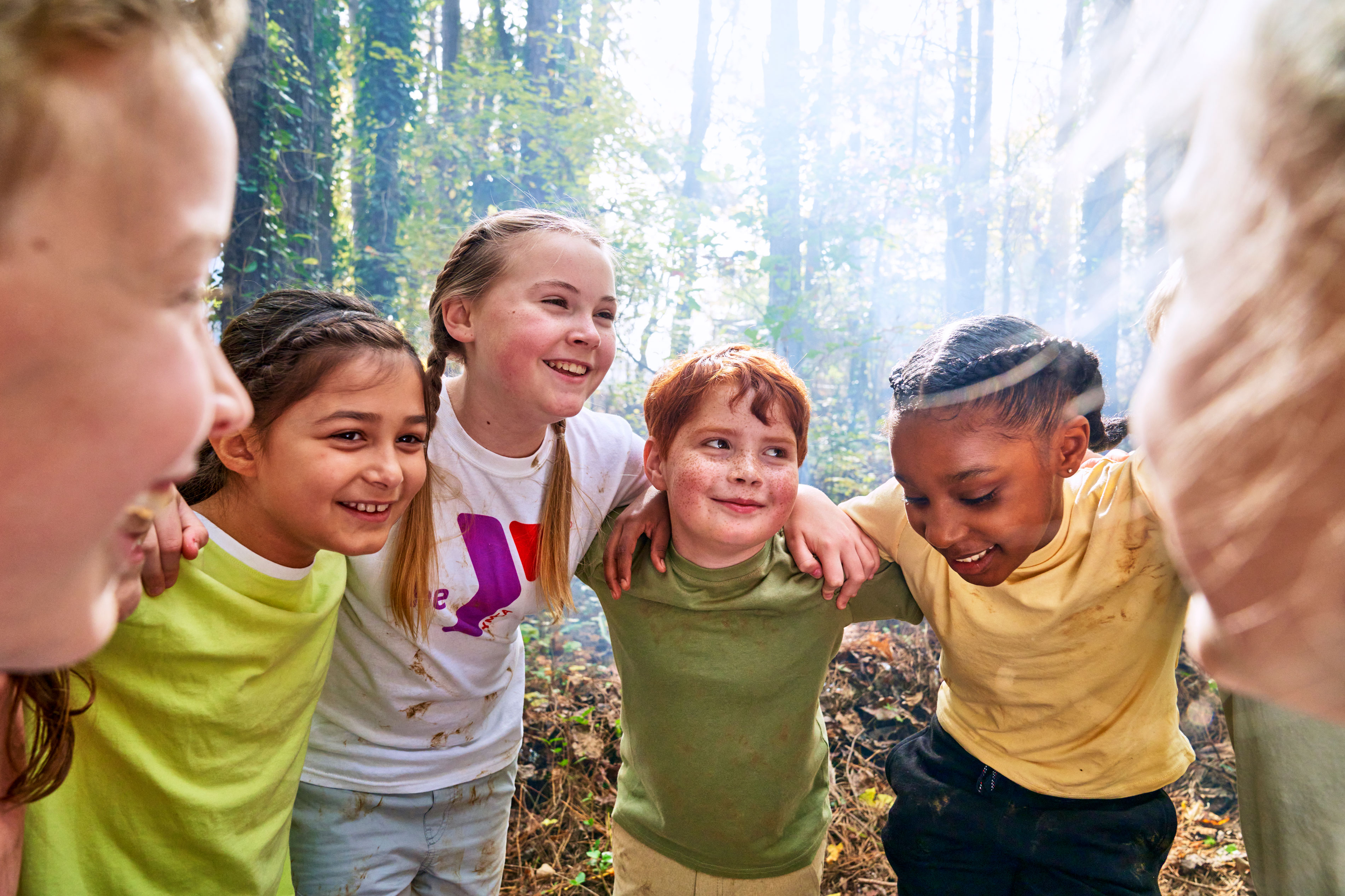 Children outdoors at day camp engaging in a group hug
