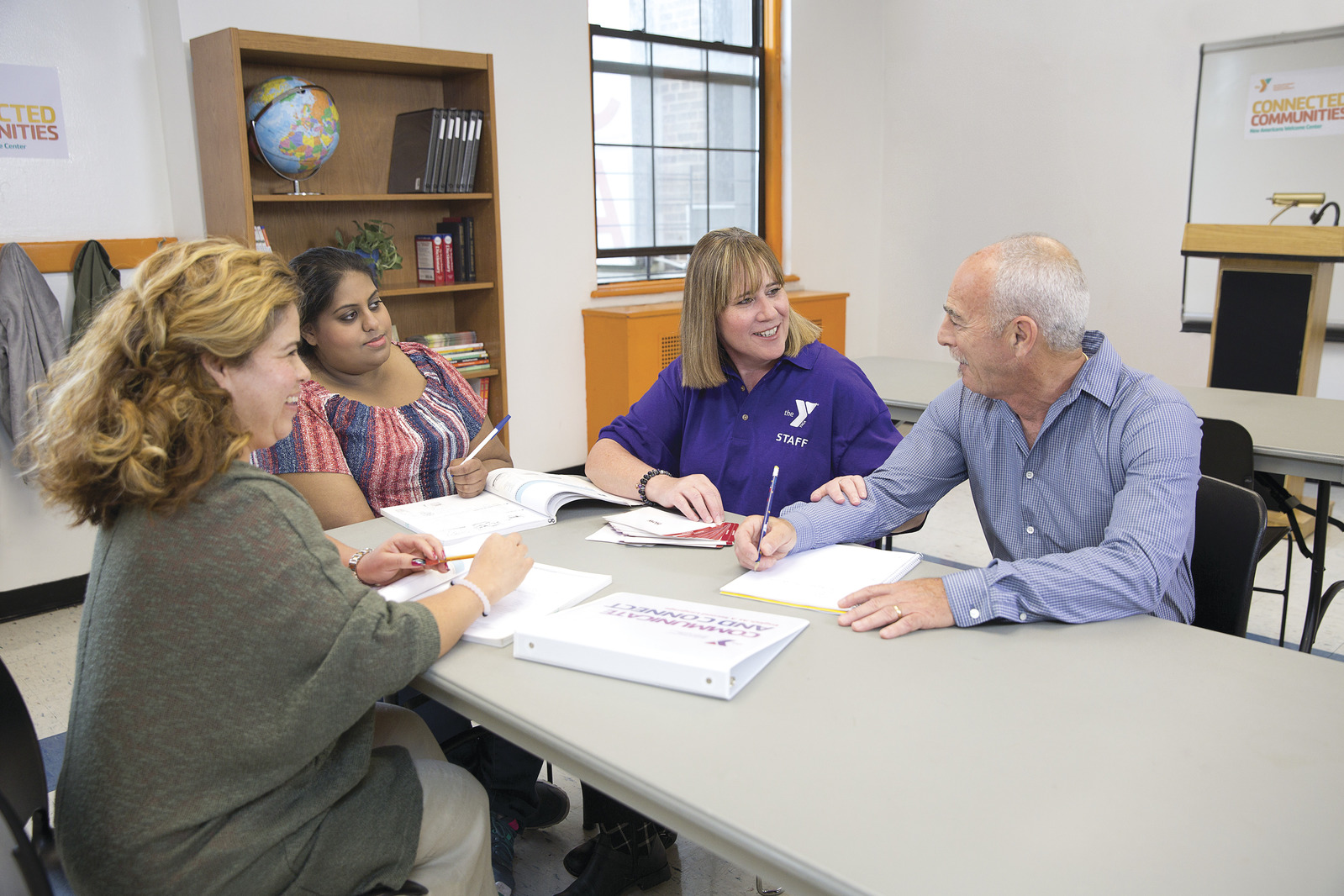 Y Staff providing newcomer resources to 3 adults in a classroom setting