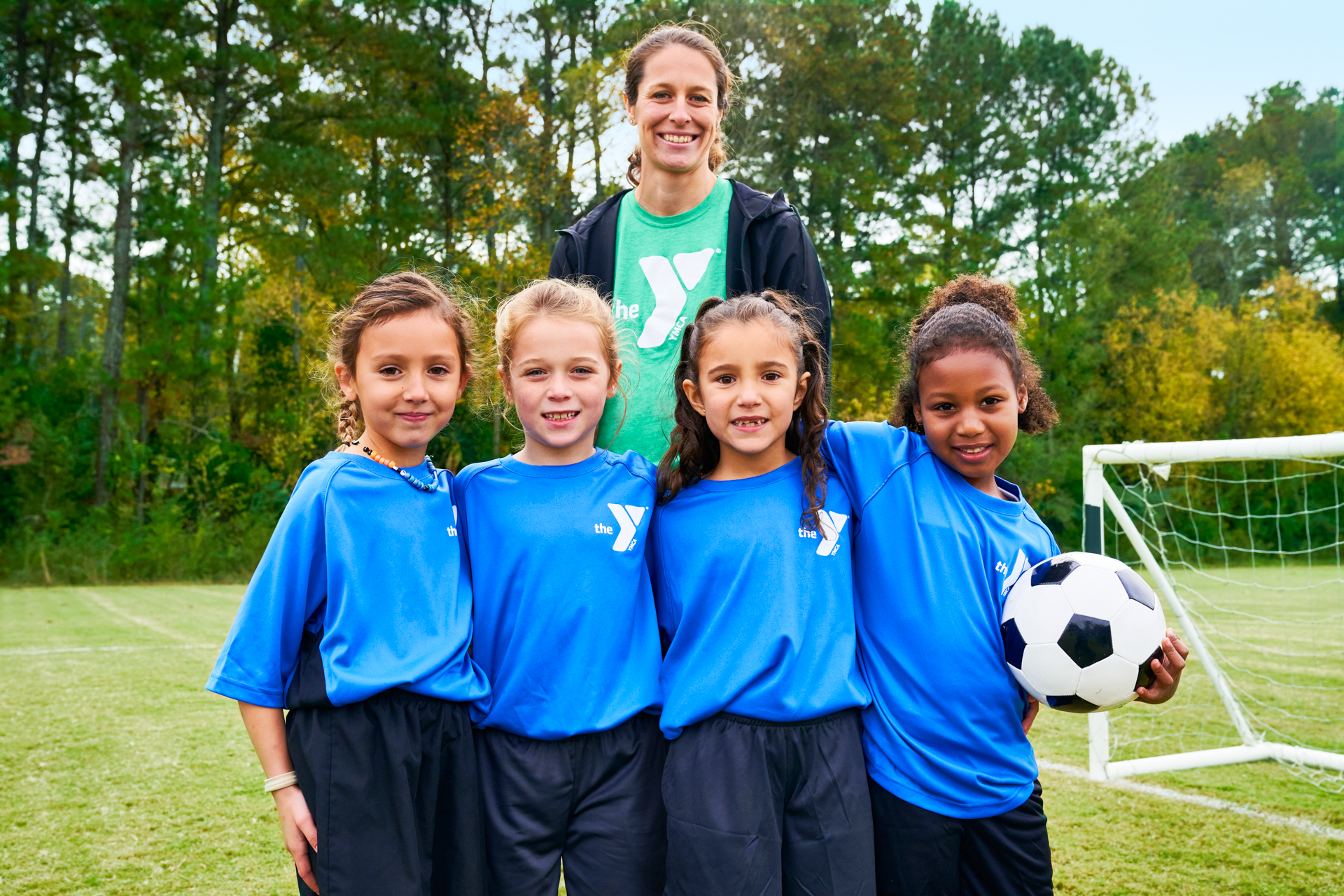 Female Y staff and 4 kids smiling at the camera during soccer practice