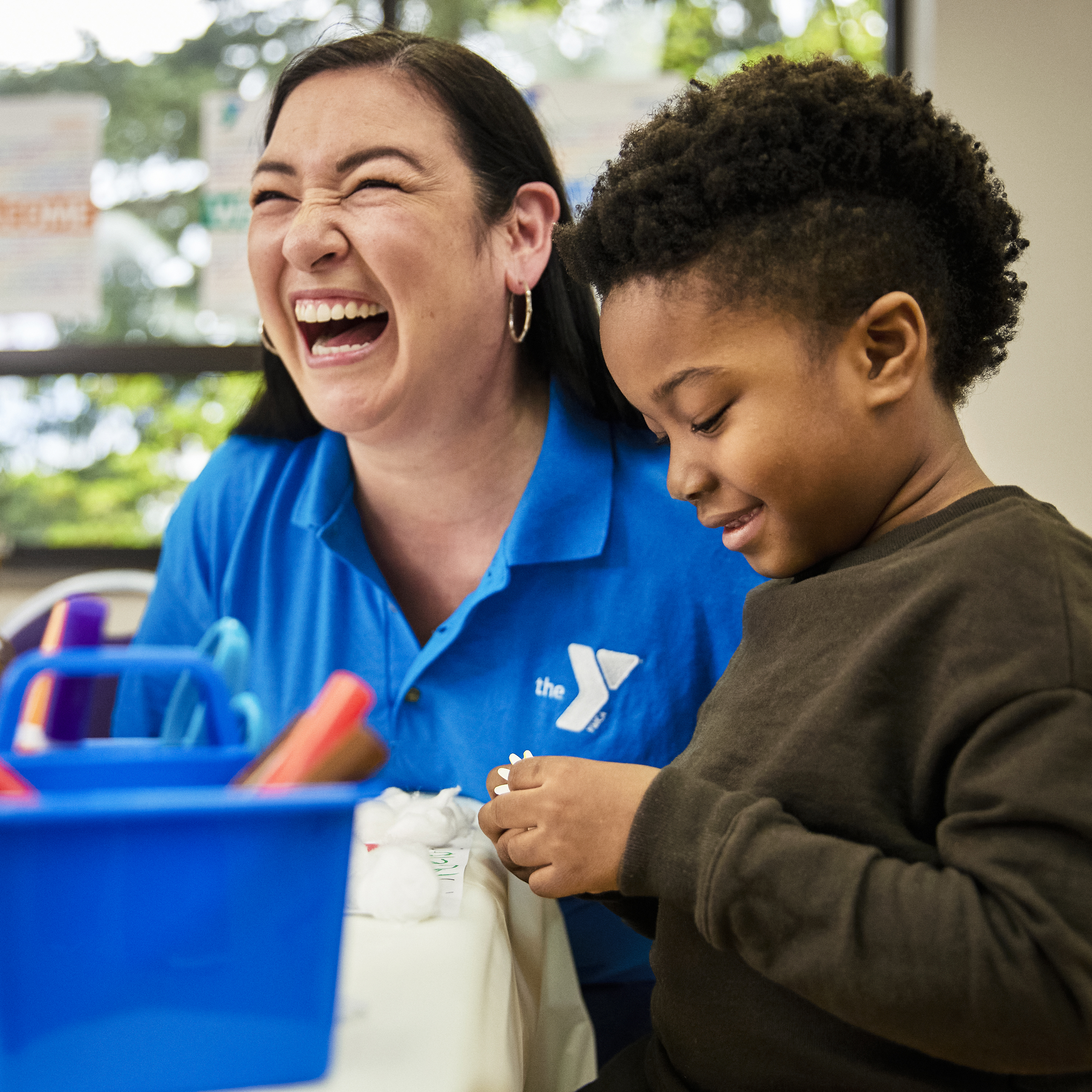 Female staff person in blue Y shirt laughing with young boy.