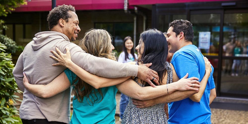 Four adults with their arms around each other shot from behind
