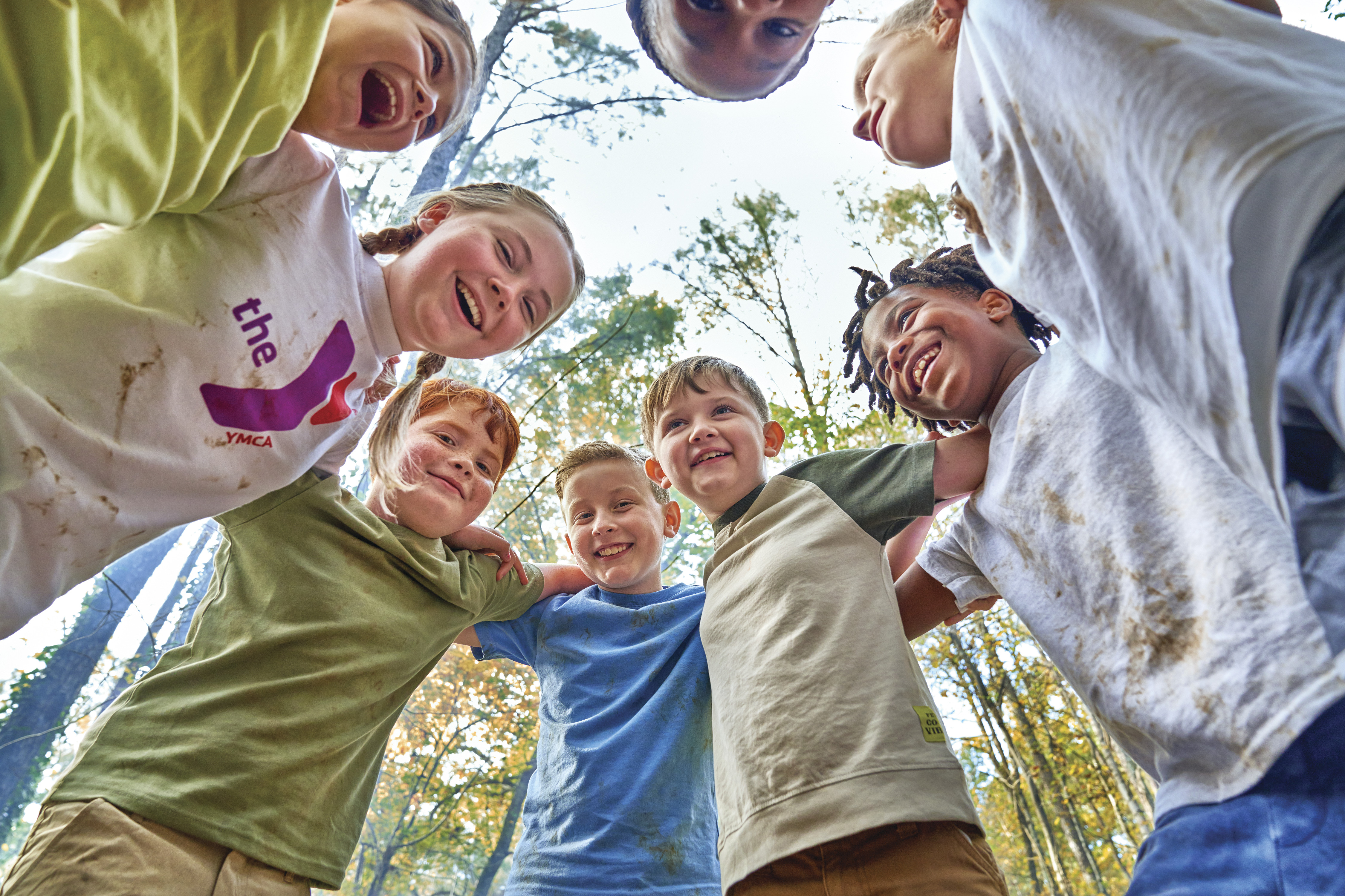 A group of YMCA youth huddle in a circle and smile at the camera