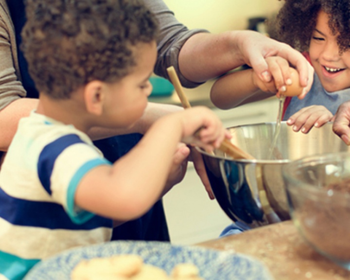 Parents helping children crack eggs into a bowl while baking