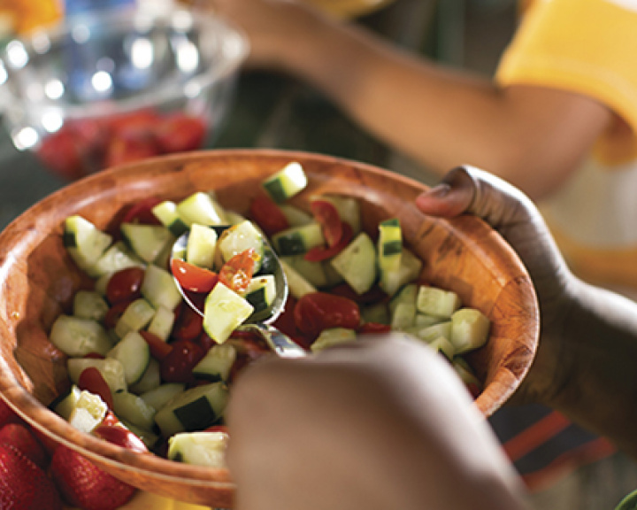 Person scooping tomato cucumber salad out of a wooden bowl