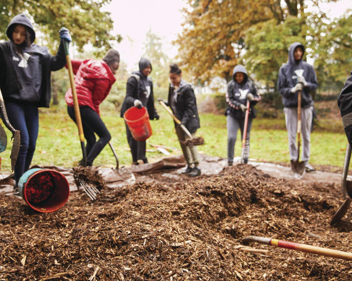 Youth in a field with gardening tools shoveling mulch